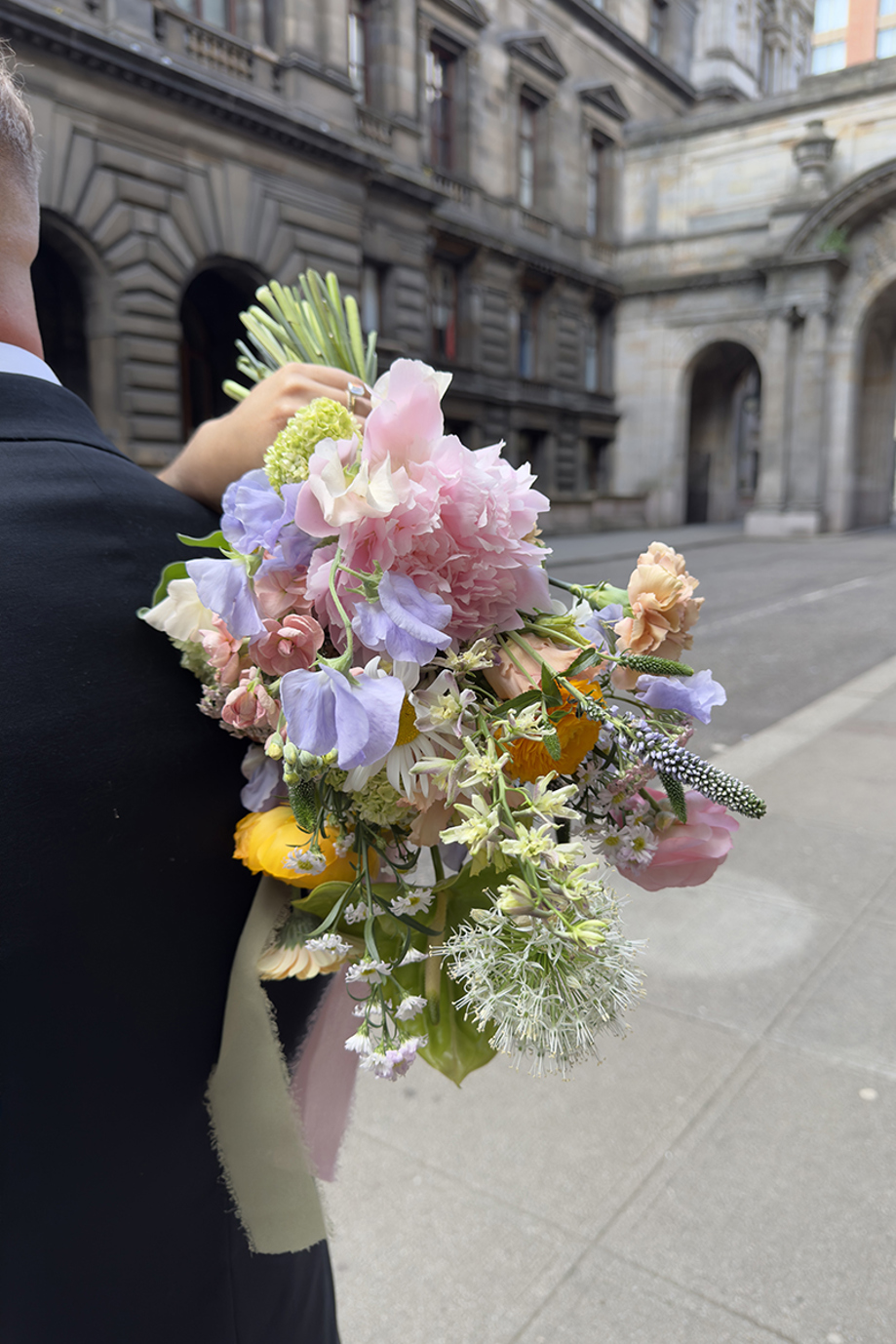 Image of grooms shoulder and brides hand holding a pastel bouquet at City Chambers in Glasgow City Centre, captured by Scottish wedding content creator, Content by Gail